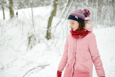 Tatlı genç kız kar yağarken güzel kış parkında eğleniyor. Karda oynayan sevimli bir çocuk. Çocuklu aileler için kış etkinlikleri.