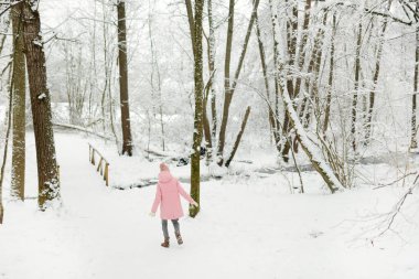 Tatlı genç kız kar yağarken güzel kış parkında eğleniyor. Karda oynayan sevimli bir çocuk. Çocuklu aileler için kış etkinlikleri.