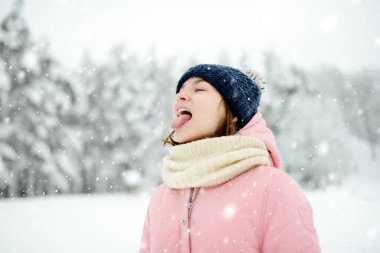 Tatlı genç kız kar yağarken güzel kış parkında eğleniyor. Karda oynayan sevimli bir çocuk. Çocuklu aileler için kış etkinlikleri.