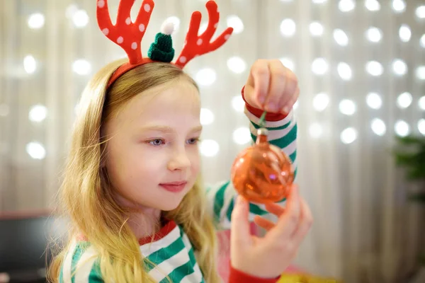 可爱的小女孩用彩色玻璃幕布装饰圣诞树 修剪圣诞树的时候在家里庆祝圣诞节 — 图库照片