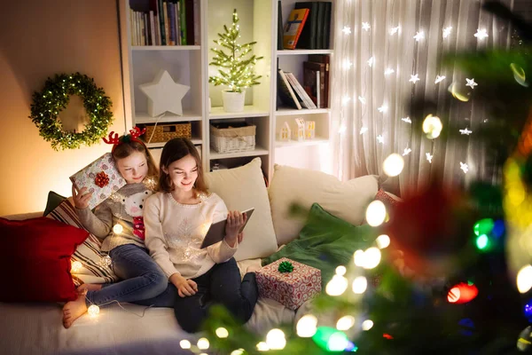 圣诞节的时候 两个可爱的妹妹在温暖舒适的客厅里用平板电脑在家里 在圣诞节前夕有网上视频通话的家庭 冬夜与家人和孩子呆在家里 — 图库照片