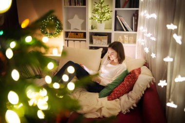 Noel 'de sıcak ve rahat oturma odasında tablet kullanan tatlı bir genç kız. Noel arifesinde ailenin online video görüşmesi var. Aile ve çocuklarla evde kış akşamı.