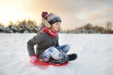 Güzel bir kış parkında kızakla eğlenen komik genç kız. Karda oynayan sevimli bir çocuk. Çocuklar için kış aktiviteleri.