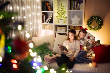 Noel 'de evde sıcak ve rahat oturma odasında tablet kullanan iki kız kardeş. Noel arifesinde ailenin online video görüşmesi var. Aile ve çocuklarla evde kış akşamı.