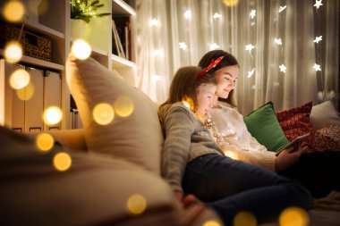 Noel 'de evde sıcak ve rahat oturma odasında tablet kullanan iki kız kardeş. Noel arifesinde ailenin online video görüşmesi var. Aile ve çocuklarla evde kış akşamı.