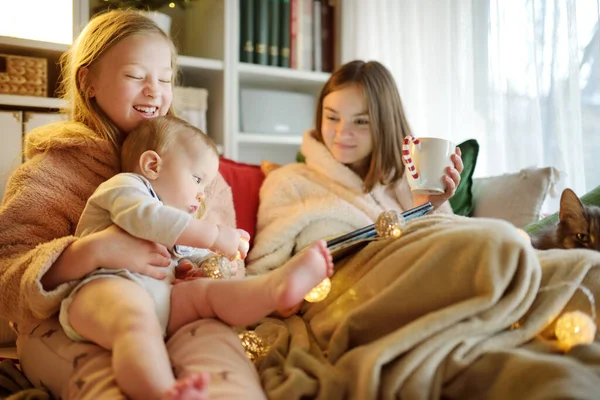 圣诞节的时候 两个妹妹和她们的小弟弟依偎在沙发上舒适的客厅里 寒假期间 可爱的孩子们在家里用平板电脑 孩子们在家里看电影 — 图库照片