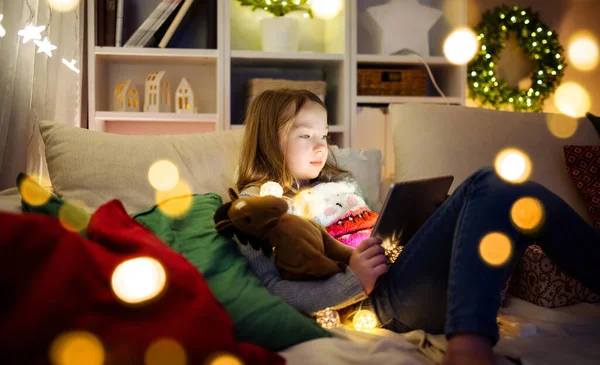 圣诞节的时候 可爱的小女孩在温暖舒适的客厅里用平板电脑在家里 在圣诞节前夕有网上视频通话的家庭 冬夜与家人和孩子呆在家里 — 图库照片