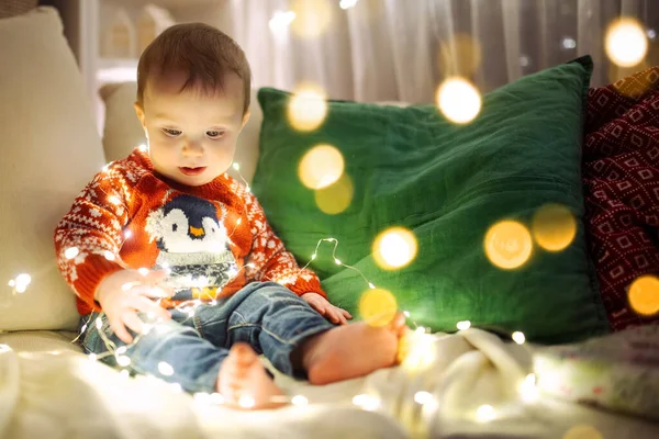 クリスマスの前夜に居心地の良いリビングルームでクリスマスライトで遊んで幸せな小さな赤ちゃんの男の子 自宅でクリスマスを祝う 家族や子供と冬の夜 — ストック写真