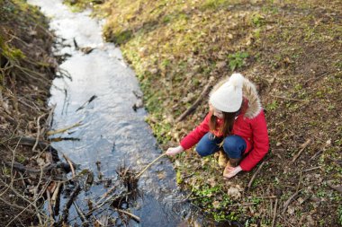Ilık bahar gününde nehir kenarında eğlenen iki kız kardeş. Çocuklar su kenarında birlikte oynuyorlar. Baharın başlarında açık hava aile aktiviteleri.
