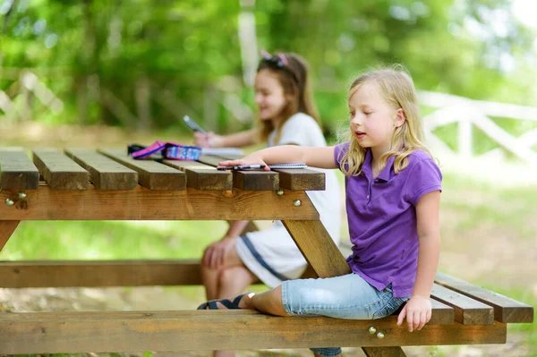 二人の幸せな姉妹が屋外の木製のテーブルで一緒に描画します 美しい夏の日に外でスケッチをする女の子 子供のための夏の活動 — ストック写真