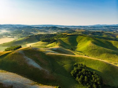 Ufukta küçük köyleri olan yeşil tarlaların ve tarım alanlarının göz kamaştırıcı manzarası. İtalya, Toskana 'nın kayan tepeleri, kıvrımlı yolları ve selvilerinin yaz manzarası.