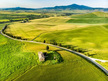 Ufukta küçük köyleri olan yeşil tarlaların ve tarım alanlarının göz kamaştırıcı manzarası. İtalya, Toskana 'nın kayan tepeleri, kıvrımlı yolları ve selvilerinin yaz manzarası.