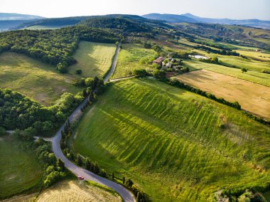 Ufukta küçük köyleri olan yeşil tarlaların ve tarım alanlarının göz kamaştırıcı manzarası. İtalya, Toskana 'nın kayan tepeleri, kıvrımlı yolları ve selvilerinin yaz manzarası.