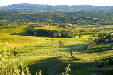 Ufukta küçük köyleri olan yeşil tarlaların ve tarım alanlarının göz kamaştırıcı manzarası. İtalya, Toskana 'nın kayan tepeleri, kıvrımlı yolları ve selvilerinin yaz manzarası.