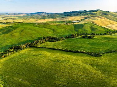 Ufukta küçük köyleri olan yeşil tarlaların ve tarım alanlarının göz kamaştırıcı manzarası. İtalya, Toskana 'nın kayan tepeleri, kıvrımlı yolları ve selvilerinin yaz manzarası.