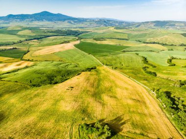 Ufukta küçük köyleri olan yeşil tarlaların ve tarım alanlarının göz kamaştırıcı manzarası. İtalya, Toskana 'nın kayan tepeleri, kıvrımlı yolları ve selvilerinin yaz manzarası.