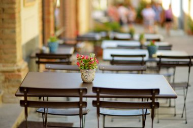 Montalcino kasabasının ortaçağ caddesinde boş bir restoran masası tepenin üstünde ve dünya çapında lezzetli şarap üretimiyle bilinen üzüm bağlarıyla çevrili. Toskana, İtalya.