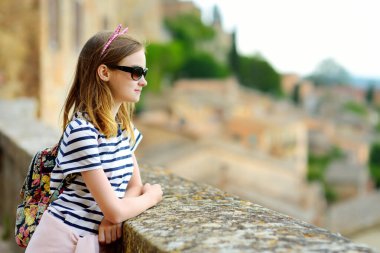 Genç kız, Tuscany 'nin yeşil tepelerini ve otlaklarını ve Montepulciano kasabasının üzüm bağlarıyla çevrili kireçtaşı bir sırtın tepesindeki çatılarını seyrediyor. Toskana, İtalya.