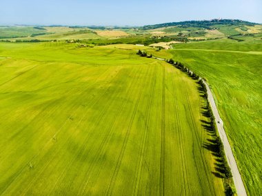 Ufukta küçük köyleri olan yeşil tarlaların ve tarım alanlarının göz kamaştırıcı manzarası. İtalya, Toskana 'nın kayan tepeleri, kıvrımlı yolları ve selvilerinin yaz manzarası.