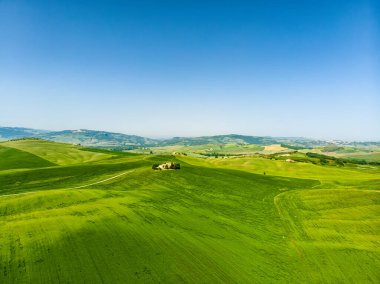 Ufukta küçük köyleri olan yeşil tarlaların ve tarım alanlarının göz kamaştırıcı manzarası. İtalya, Toskana 'nın kayan tepeleri, kıvrımlı yolları ve selvilerinin yaz manzarası.