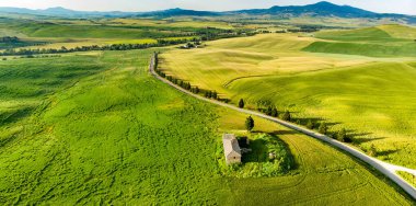 Ufukta küçük köyleri olan yeşil tarlaların ve tarım alanlarının göz kamaştırıcı manzarası. İtalya, Toskana 'nın kayan tepeleri, kıvrımlı yolları ve selvilerinin yaz manzarası.