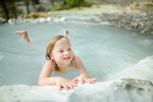 Young girl bathing in Bagni San Filippo, small hot spring containing calcium carbonate deposits, which form white concretions and waterfalls. Geothermal pools and hot springs in Tuscany, Italy.