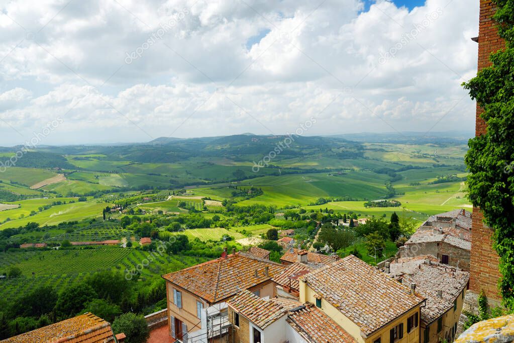 Green hills and pastures of Tuscany and rooftops of Montepulciano town, located on top of a limestone ridge surrounded by vineyards. Vino Nobile wine territory. Tuscany, Italy.