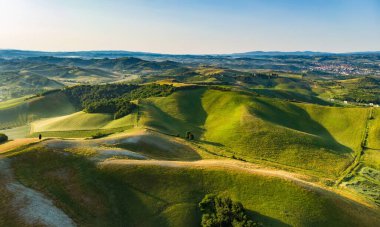 Ufukta küçük köyleri olan yeşil tarlaların ve tarım alanlarının göz kamaştırıcı manzarası. İtalya, Toskana 'nın kayan tepeleri, kıvrımlı yolları ve selvilerinin yaz manzarası.