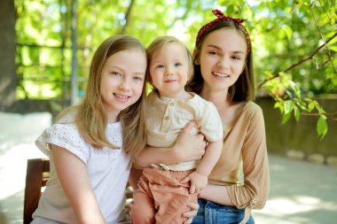 İki abla ve küçük erkek kardeşleri dışarıda eğleniyorlar. Yaz günü kucağında iki genç kız. Geniş yaş farkı olan çocuklar. Kardeşler arasında büyük yaş farkı var. Büyük aile..