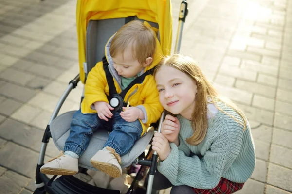 姉と弟は屋外のベビーカーに座っていました 幼児はプッシュチェアで 春は子供たちと歩く 小さな子供と家族のレジャー — ストック写真