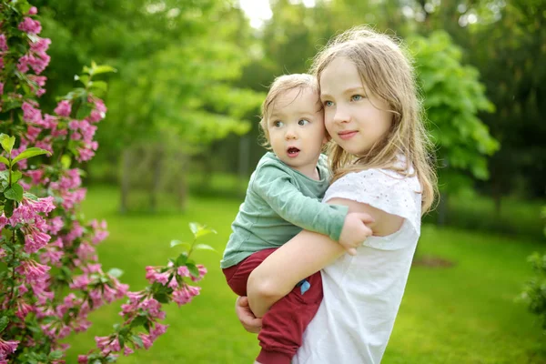 姉と妹の弟は屋外で楽しんでいます 春の日に赤ん坊の男の子と遊んでいる若い女の子 年齢差の大きい子供たち 兄弟間の大きな年齢差 — ストック写真