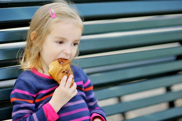 Adorable Niña Comiendo Croissant Recién Horneado Mientras Sienta Banco Día — Foto de Stock