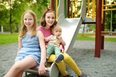 Küçük tatlı çocuk, sıcak bir yaz gününde oyun bahçesinde ablalarıyla eğleniyor. Yazın çocuklar için aktif eğlence.