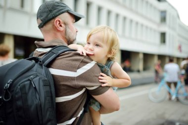 Babasının kollarında tatlı bir çocuk var. Baba ve oğul güneşli bir yaz gününde şehirde eğleniyorlar. Sevimli bebek babası tarafından tutuluyor..