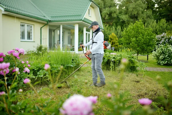 中年男子在后院用电动或汽油草坪修剪高草 照料工具和设备的园艺 用割草机修剪草坪的工艺 — 图库照片