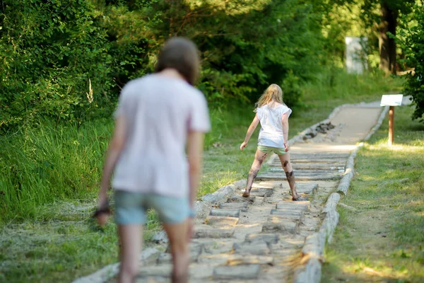 Two sisters on tactile path in barefoot park created to feel the ground and other materials with bare feet. Strengthen foot and leg muscles by walking on uneven surface in a park environment.