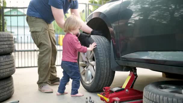 かわいい幼児の少年は 父親が裏庭で車の車輪を変えるのを助けています 父は息子に道具の使い方を教える 小さな子供のアクティブな親 — ストック動画