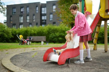 Küçük tatlı bir çocuk, sıcak bir sonbahar gününde oyun parkında ablasıyla eğleniyor. Sonbaharda çocuklar için aktif eğlence.