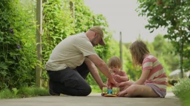 Young father fixing a skateboard for his young daughter. Pretty little girl learning to skateboard on beautiful summer day in a park. Child enjoying skateboarding ride outdoors.