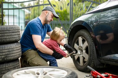 Tatlı çocuk, babasının arka bahçesinde araba tekerleklerini değiştirmesine yardım ediyor. Baba küçük oğluna alet kullanmayı öğretiyor. Küçük bir çocuğun aktif ebeveyni.