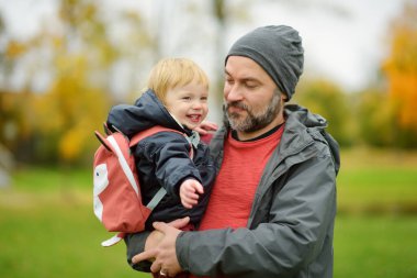 Babasının kollarında tatlı bir çocuk var. Baba ve oğul güneşli bir sonbahar gününde eğleniyorlar. Babası tarafından tutulan sevimli bir oğul. Sonbahar mevsiminde aktif aile zamanı.