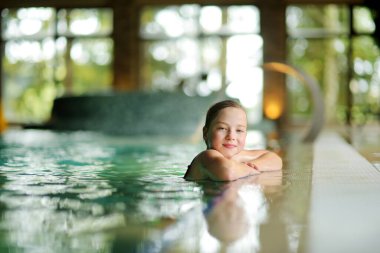 Şirin genç kız kapalı havuzda eğleniyor. Çocuk yüzmeyi öğreniyor. Çocuk su oyuncaklarıyla eğleniyor. Havuzda aile eğlencesi. Çocuklu aile aktiviteleri.