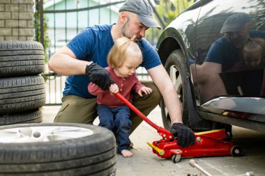 Tatlı çocuk, babasının arka bahçesinde araba tekerleklerini değiştirmesine yardım ediyor. Baba küçük oğluna alet kullanmayı öğretiyor. Küçük bir çocuğun aktif ebeveyni.