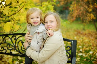 Komik çocuk ve ablası güneşli bir sonbahar gününde dışarıda eğleniyorlar. Doğayı keşfeden çocuklar. Şehir parkında yürüyen çocuklar. Küçük çocuklar için sonbahar aktiviteleri.