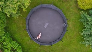 Aerial top-down view of a teenage girl jumping on trampoline in a backyard. Backyard kids fun. Summer outdoor leisure activities.