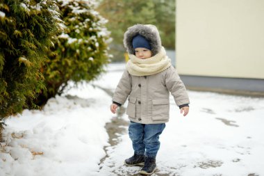 Tatlı çocuk, kar yağışlı kış gününde arka bahçede eğleniyor. Karda oynayan, kalın giysiler giymiş şirin bir çocuk. Çocuklu aileler için kış etkinlikleri.