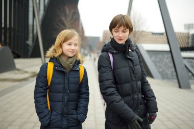 Soğuk kış sabahında sırt çantalı şirin kız kardeşler okula gidiyor. Çocuklar okula geri dönüyor. Çocuklar için eğitim.