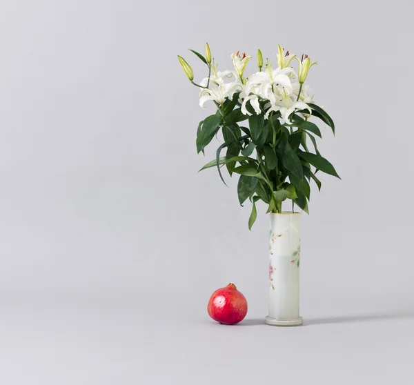Білі лілії у вазі та червоному гранаті . — стокове фото