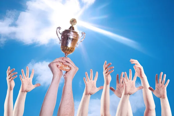 Hand van de persoon met de kop van een sport op een achtergrond van de heldere hemel. — Stockfoto