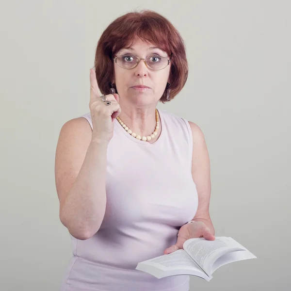 An elderly woman with a book emphasizes the viewer. — Stock Photo, Image